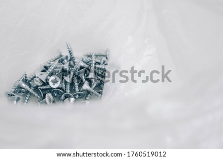 Small metal screws in plastic bag on white wooden background. Construction equipment concept. Top view. Copy, empty space for text
