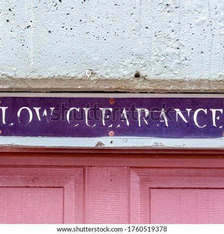 Square crop Low Clearance sign above the panelled red wooden garage door of a building