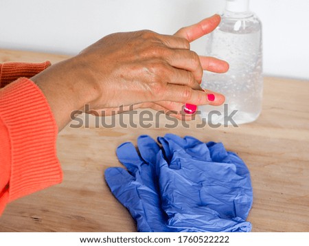 close up of  adult woman hands while cleaning and sanitizing  herself  with anti virus bacterial gel against covid-19 , fall dress, orange color over a wood table, earth tones.