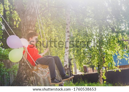 A teenage boy in a red t-shirt swings on a swing in a Park in the summer. The child is resting, school holidays.