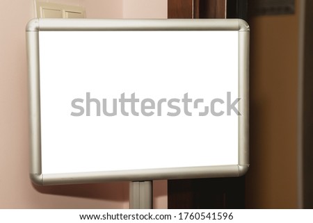Empty layout of framed wall poster. White insulation frame template in front of door against wall. Layout of front view of blank Billboard for your information in gray frame for your label or image