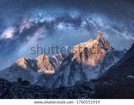 Arched Milky Way over the beautiful mountains at night in Himalayas, Nepal. Colorful space landscape with blue starry sky with Milky Way arch, snowy mountain peak. Galaxy, stars and rocks. Nature