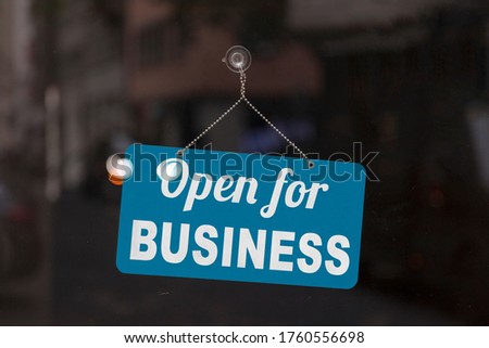 Close-up on a blue open sign in the window of a shop displaying the message: Open for business.
