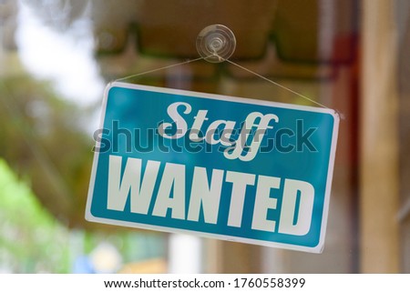 Close-up on a blue open sign in the window of a shop displaying the message: Staff wanted.