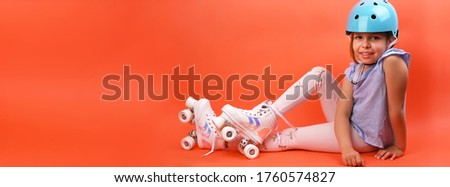 A small child with roller skates and a blue helmet demonstrates positive emotions. A girl of 7 years old poses and prepares for active leisure on retro ice skates. Children's sport concept.Copy space