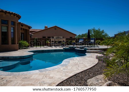 A travertine patio with a pebble tech pool in a desert landscaped backyard. Royalty-Free Stock Photo #1760577950