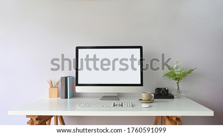 Working desk is surrounding by a white blank screen computer monitor and office equipment.