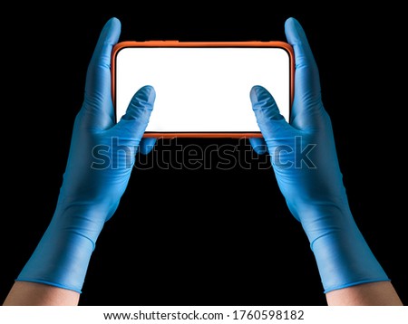 Doctor's hand in sterile medical gloves holding phone playing games isolated on black background with clipping path. Concept of protection against pandemic and viruses