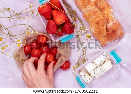 Light lunch outdoors. Baguette, blue cheese, cherry tomatoes and strawberry on tablecloth. Top view.