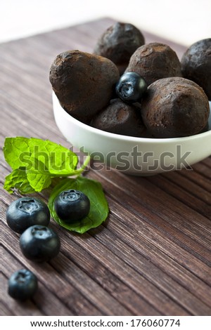 Chocolate truffles in white porcelain bowl with blueberry and leaf of mint on wooden background