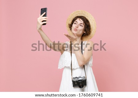 Cute tourist girl in dress hat photo camera isolated on pink background. Traveling to travel weekends getaway. Air flight journey concept. Doing selfie shot on mobile phone, blowing sending air kiss
