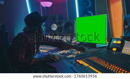 Stylish Audio Producer Working in Music Record Studio, Uses Green Screen Chroma key Computer Display, Mixer Board Equalizer and Control Desk to Create New Hit Song. Creative Black Artist Musician