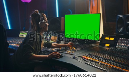 Stylish Female Audio Engineer / Producer Working in Music Record Studio, Uses Headphones, Green Screen Computer Display, Mixer Board, Control Desk to Create New Song. Creative Artist Musician.