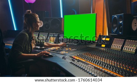 Portrait of Stylish Female Audio Engineer / Producer Working in Music Record Studio, Uses Green Screen Computer Display, Mixer Board, Control Desk to Create New Song. Creative Artist Musician
