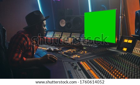 Stylish Audio Engineer / Producer Working in Music Record Studio, Uses Green Screen Chroma key Computer Display, Mixer Board Equalizer and Control Desk to Create New Hit Track and Song. Black Musician