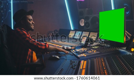Stylish Audio Engineer / Producer Working in Music Record Studio, Uses Green Screen Chroma key Computer Display, Mixer Board Control Desk to Create New Hit Track, Song. Creative Black Artist Musician