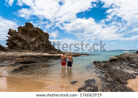 Ocean coastline beach with rocky headland landmark into blue waters couple in shallow tidal cove 