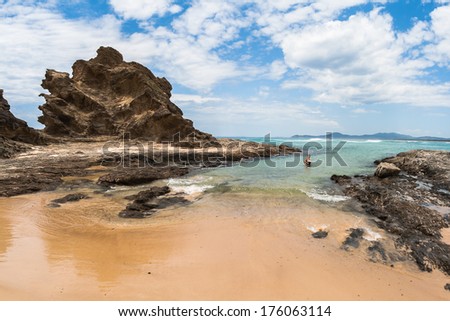 Ocean coastline beach with rocky headland landmark into blue waters with woman swimming in shallow tidal cove 