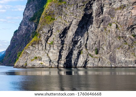 Vertical, steep rocks are washed by the waters of the fjords. The texture of the stone emphasizes the contrasting light of the sun.