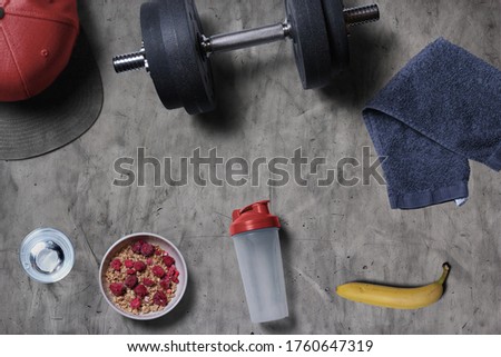 Gym scene with dumbbell weights cereal water bottle towel banana and cap