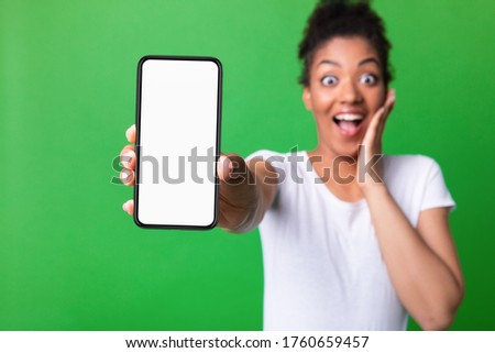 Amazed Black Girl Showing Blank White Smart Phone Screen, Looking At Camera Isolated Over Green Studio Wall