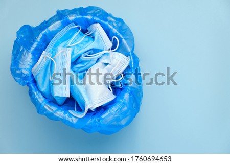 Mask thrown in the trash. Discarded surgical masks. Medical waste with copy space on a blue background. Over of coronavirus, SARS-CoV-2 pandemic. Royalty-Free Stock Photo #1760694653