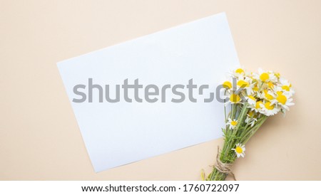 Wedding desktop mock up with blank white paper card and chamomiles flowers bouquet branch on beige background.Empty copy space.Styled stock photo,web banner.Flat lay,top view.Spring or summer concept