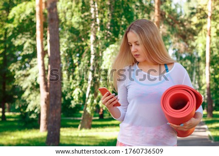 Gorgeous Woman Carrying a Yoga Mat Outdoors Early Morning and Read Text Messages on Smartphone