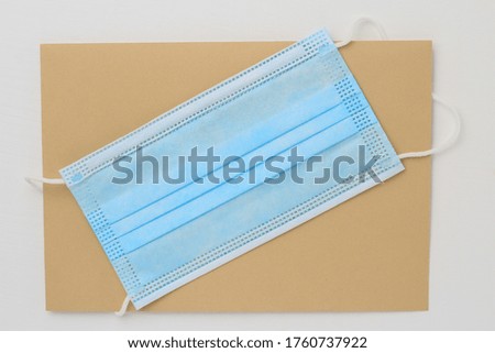 A medical surgical mask lies on a classic postal envelope. White wood background