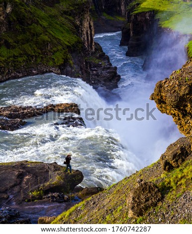 Iceland. Gullfoss "Golden Falls" - the waterfall fed by glacial water. Tourist - photographer with photo bag  takes pictures of burrowing waterfall. The concept of extreme and photo tourism