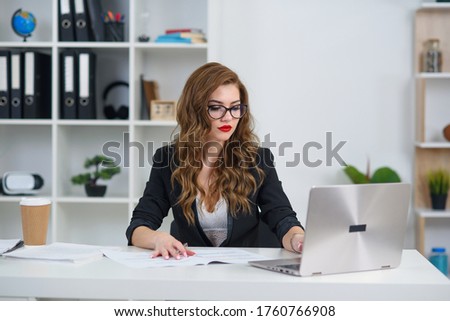 Attractive caucasian businesswoman sitting at desk in cozy bright office and working with laptop computer.