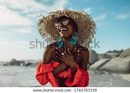 Beautiful african woman in red dress wearing straw hat smiling on the beach. Female in sundress enjoying on the beach. Royalty-Free Stock Photo #1760783198