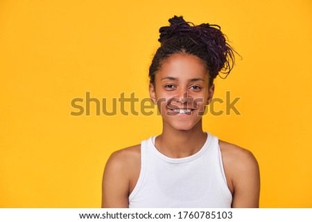Young happy dark skinned teenager girl in white T-shirt isolated on yellow background. Positive african woman smiles happily, expresses sincere emotions, has fun with each other. Copy space.