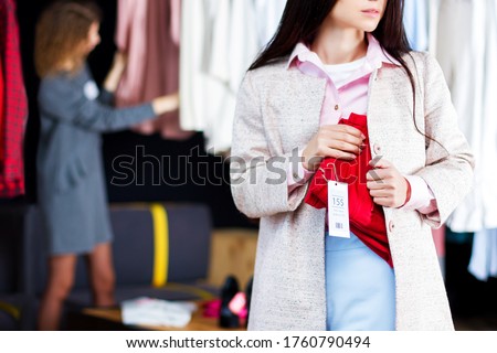 Closeup of young woman is stealing red jeans in store, shop, boutique at shopping center. Girl is hiding unpaid good under clothes. Seller, assistant caught thief on hot. Shoplifting concept. Royalty-Free Stock Photo #1760790494
