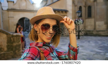 Portrait of young stylish woman in sun glasses posing while making photo on the camera in the city street.