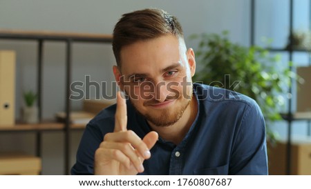 Portrait of emotional funny man moving his fingers at the camera on the grey office background.