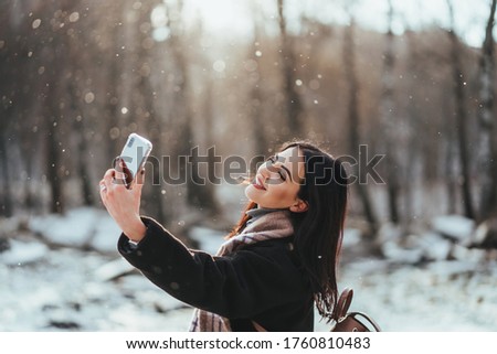 happy smiling teenage girl or young woman taking selfie by smartphone in winter park