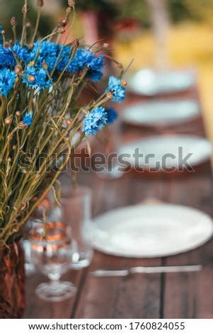 Close up of blue cornflowers in a vase on a dinner table. Blurred background. Midsummer flowers from a meadow. Empty dishes set on a table  Royalty-Free Stock Photo #1760824055