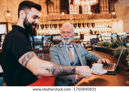  Waiter serving drink to mature businessman in restaurant.