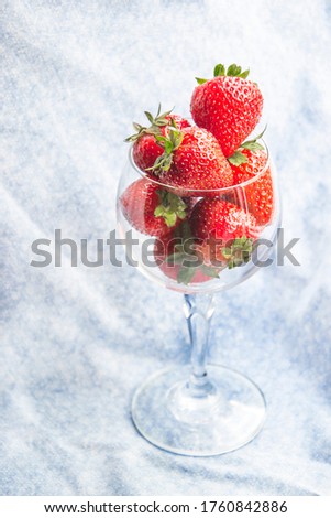 Close up picture of glass with strawberries on blue background. Copy space concept with flat lay composition. Summer period of time with fresh berries. Wallpaper with fruits in sheer glass.