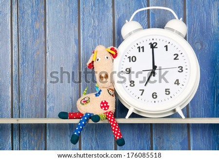 Stuffed animal Giraffe sitting next to alarm clock at seven o'clock isolated over white background