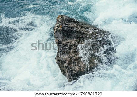 Big stone in azure water of mountain river close-up. Blue nature background with big boulder in turquoise water of mountain creek. Full frame of sea surf. Ocean surf among stones. Backdrop of tide.
