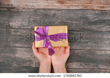 The girl holds out a gift box with a top view. Hands hold gift box on a wooden background. View from above. Flat lay.