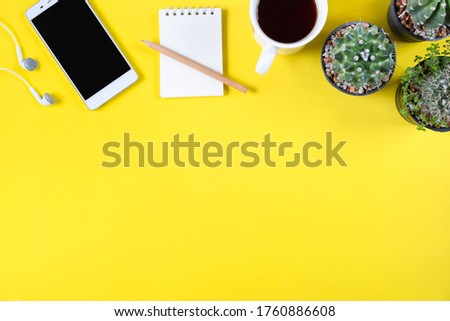 Top view of smartphone, cactus plants, cup of coffee, and mini notebook on yellow background
