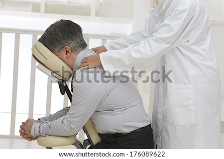 Businessman sitting on massage chair, getting shoulder massage.