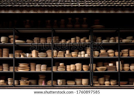 Group of handcraft ceramic kitchenwares arranged on shelve in warehouse pottery workshop studio. Royalty-Free Stock Photo #1760897585