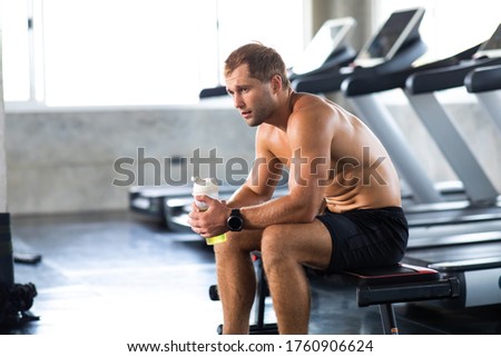 sportsman  taking a break after running on treadmill machine at the gym sitting  and drinking gatorade water at sport club. Fitness Healthy lifestye and workout at gym concept.