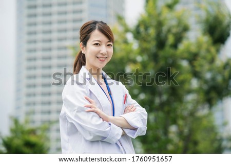 Asian female healthcare worker in white coat posing outdoors