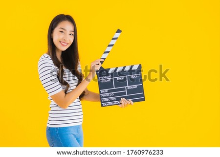 Portrait beautiful young asian woman show clapper movie board on yellow isolated background