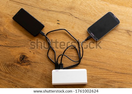 Two Mobile Phone sharing USB Power Bank on a wooden Table to charge the moblie devices